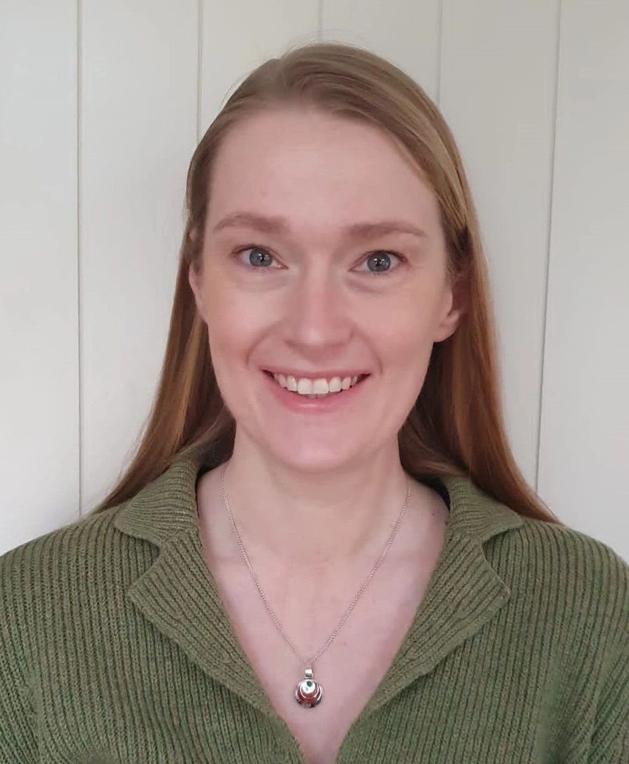 Natalie Gibellini smiling, wearing a green sweater and pendant necklace