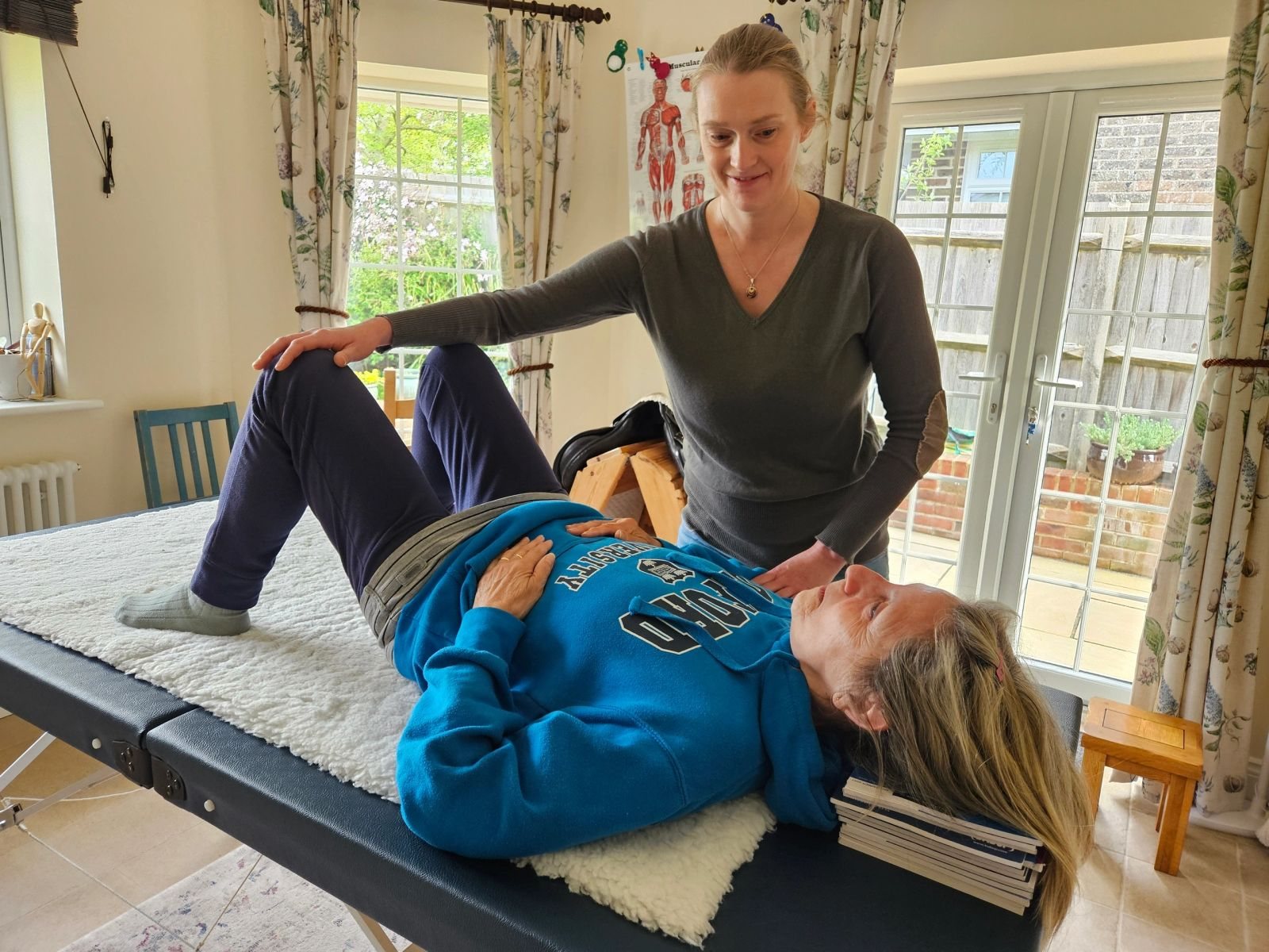 Natalie guiding a client who is lying in semi-supine on a teaching table, knees bent and head resting on a stack of books, in her Seaford studio